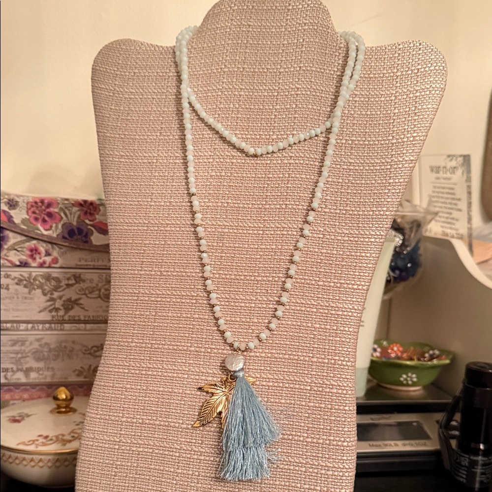 long, light blue aquamarine beaded necklace with a tassel and charm accents
